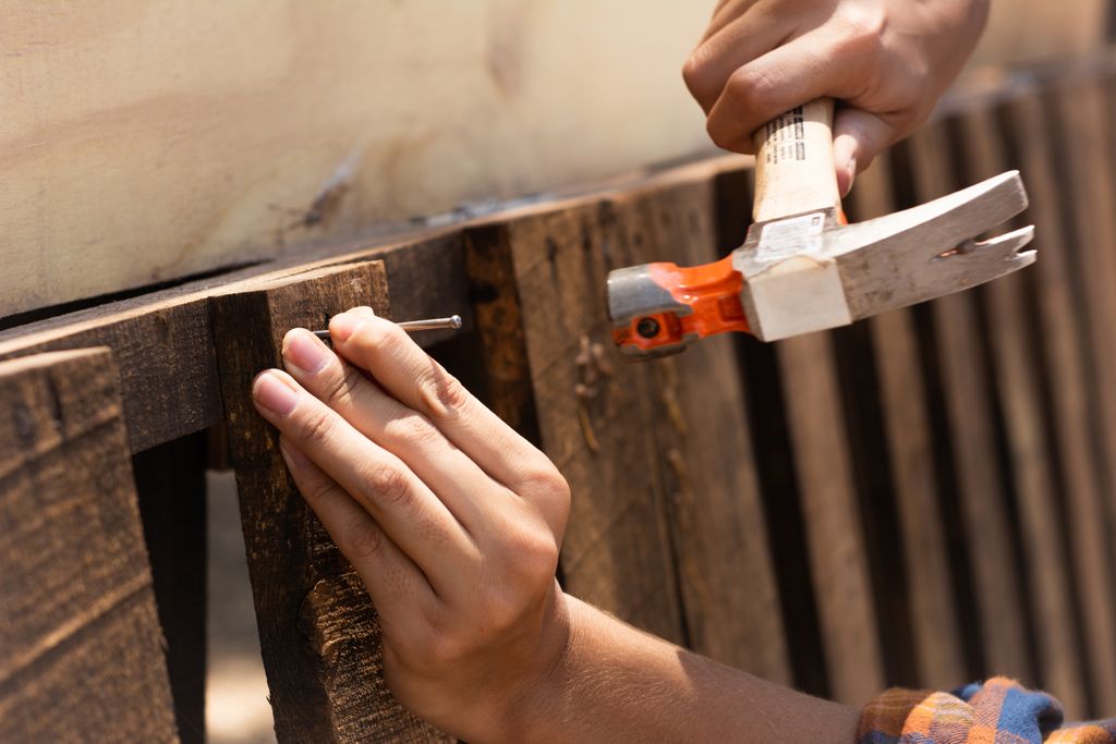 A detailed image showing hands hammering a nail into wooden planks, emphasizing carpentry work.